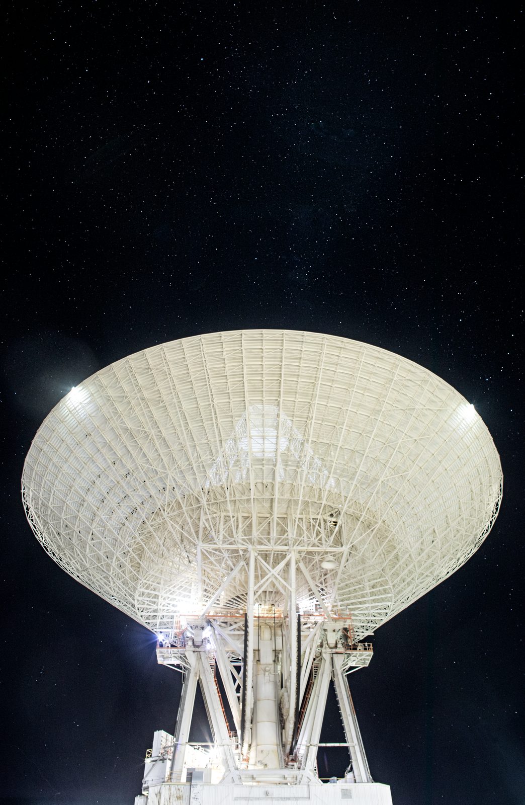 Una antena parabólica enorme apuntando al cielo, recortada bajo un firmamento lleno de estrellas.