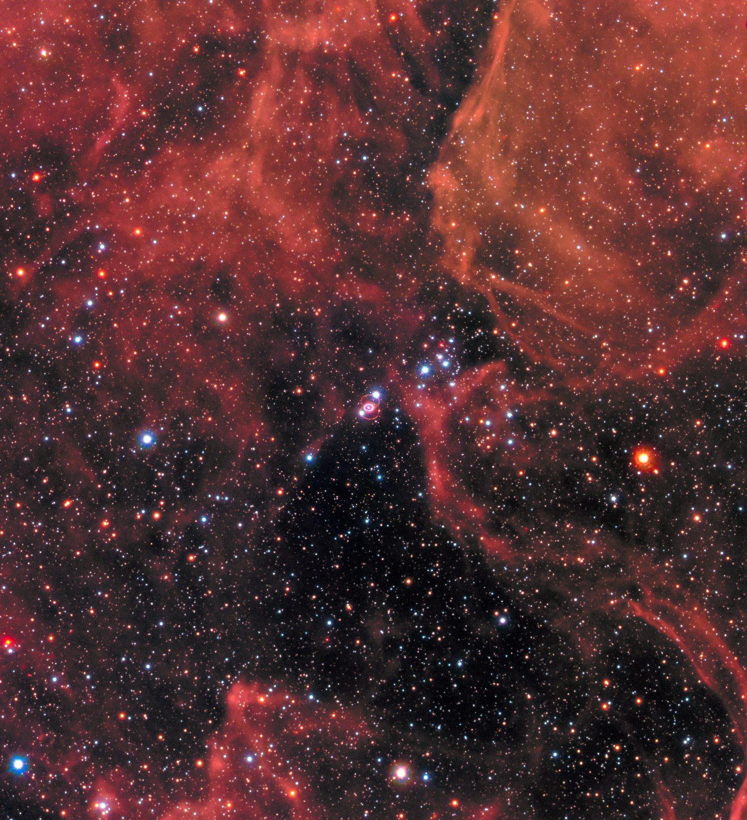 Un campo rojizo de nebulosa sembrado de cientos de estrellas; casi en el centro, un anillo diminuto y brillante: los restos de la supernova 1987A.
