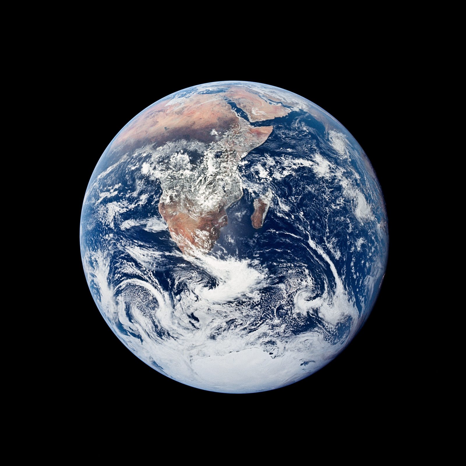 El disco completo de la Tierra sobre el negro del espacio: África y la Península Arábiga a la izquierda, el casquete blanco de la Antártida abajo y grandes espirales de nubes.