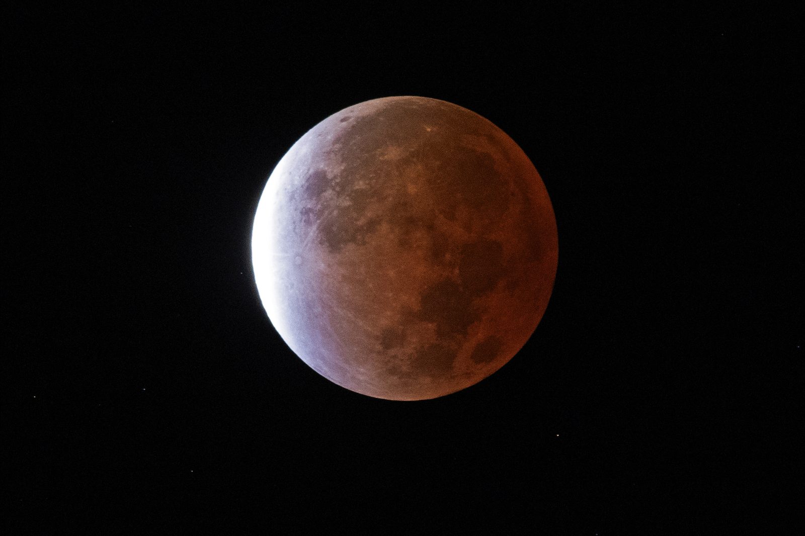 La Luna casi completamente cubierta por una sombra cobriza, con un filo blanco muy brillante en uno de sus bordes.