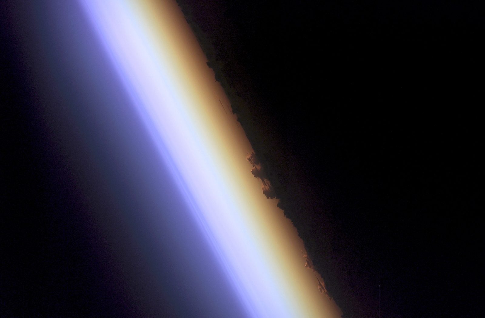 El borde curvo de la Tierra visto desde la órbita, con una franja luminosa naranja y roja bajo capas azules cada vez más oscuras.