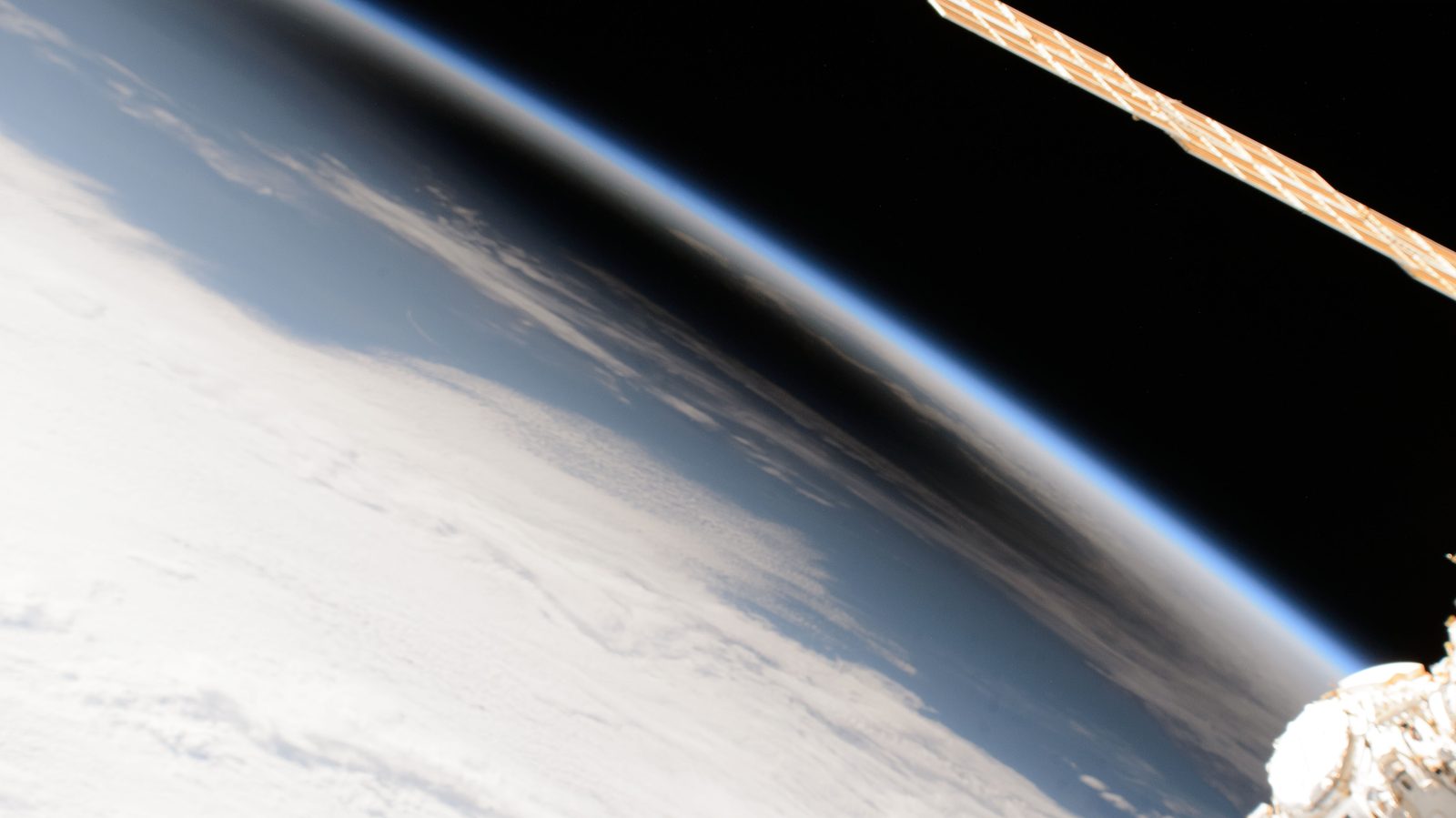 La curva de la Tierra vista desde la órbita, con una mancha oscura y difusa apoyada sobre las nubes.