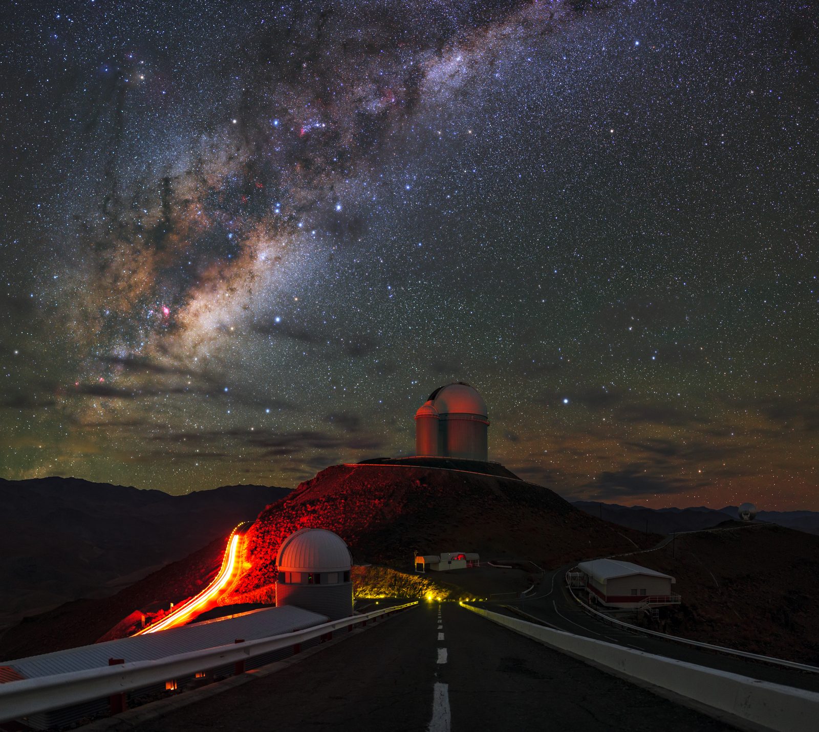 Una cúpula de observatorio sobre un cerro oscuro, con la banda de la Vía Láctea levantándose detrás en el cielo.