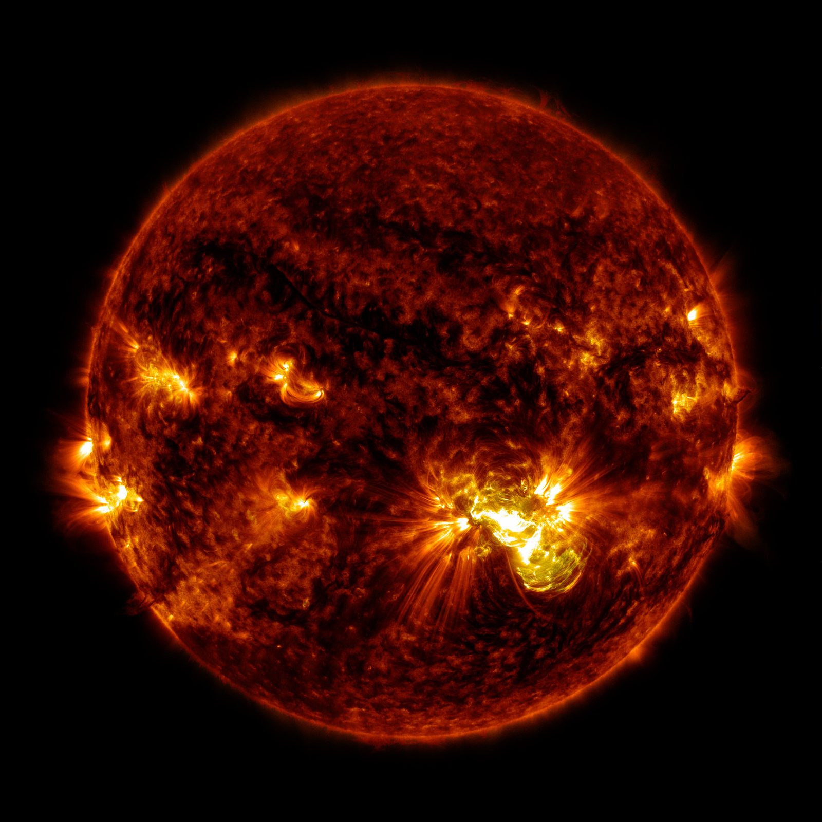 El disco completo del Sol en tonos rojos y anaranjados, con una región activa deslumbrante y varios penachos brillantes en el borde.