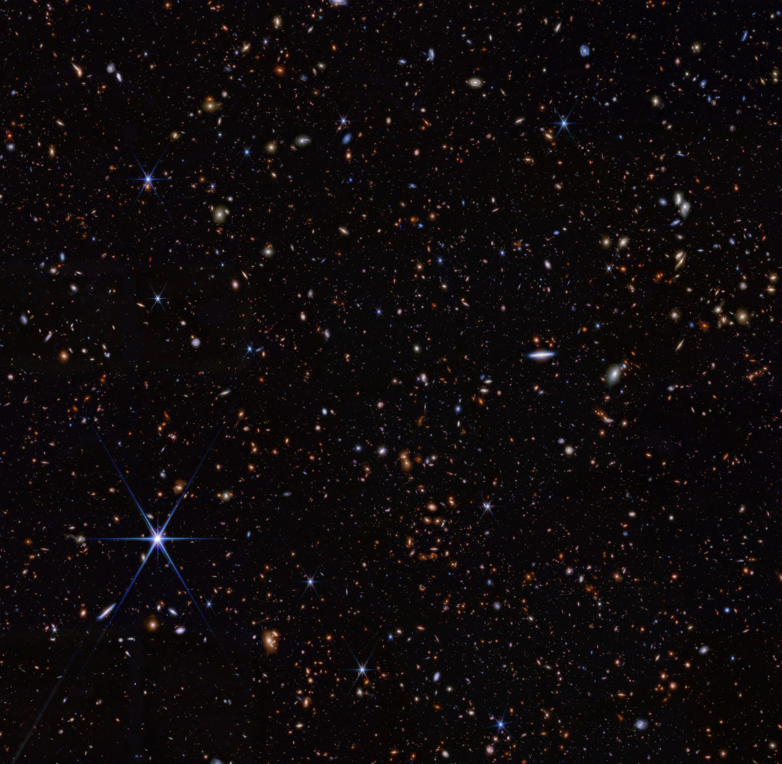 Miles de galaxias pequeñas de todos los colores y formas repartidas sobre el fondo negro del espacio, con una estrella brillante de primer plano abajo a la izquierda.
