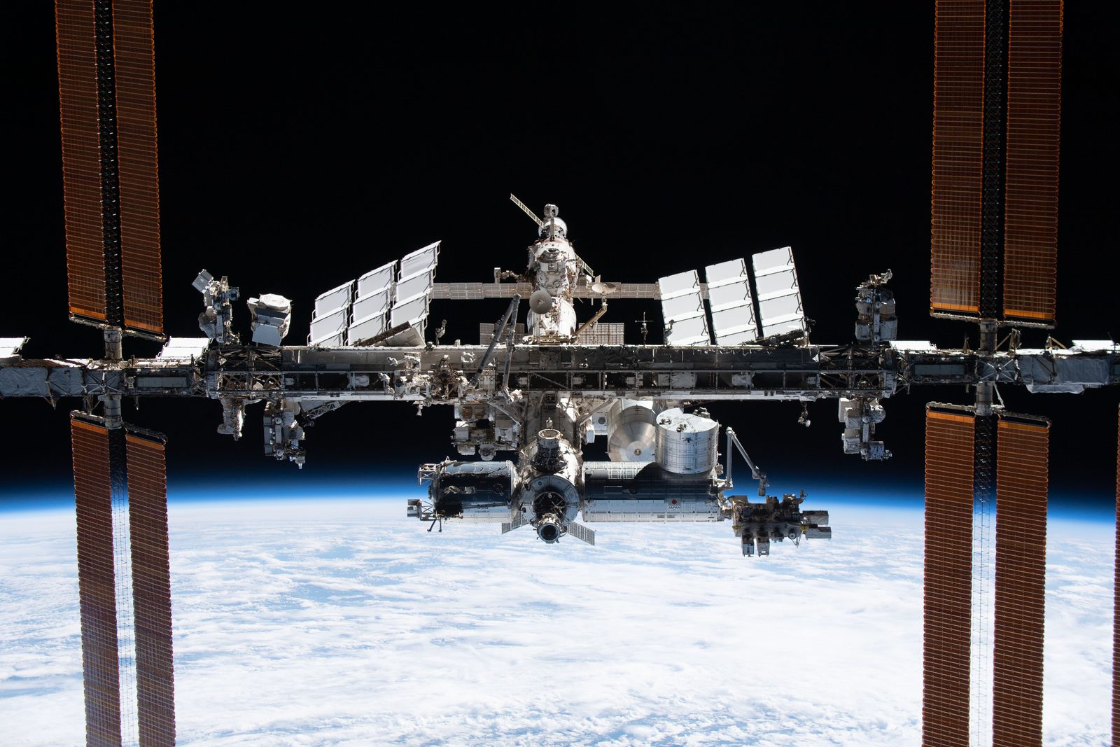 La Estación Espacial Internacional con sus módulos y paneles solares desplegados, con la Tierra debajo.