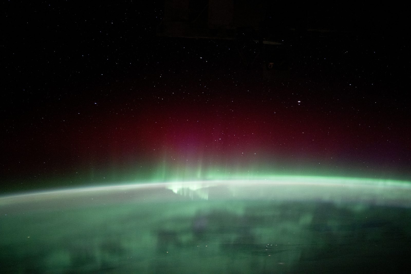Arco verde de aurora boreal extendido sobre el limbo curvo de la Tierra, con la atmósfera en capas y el cielo estrellado encima.
