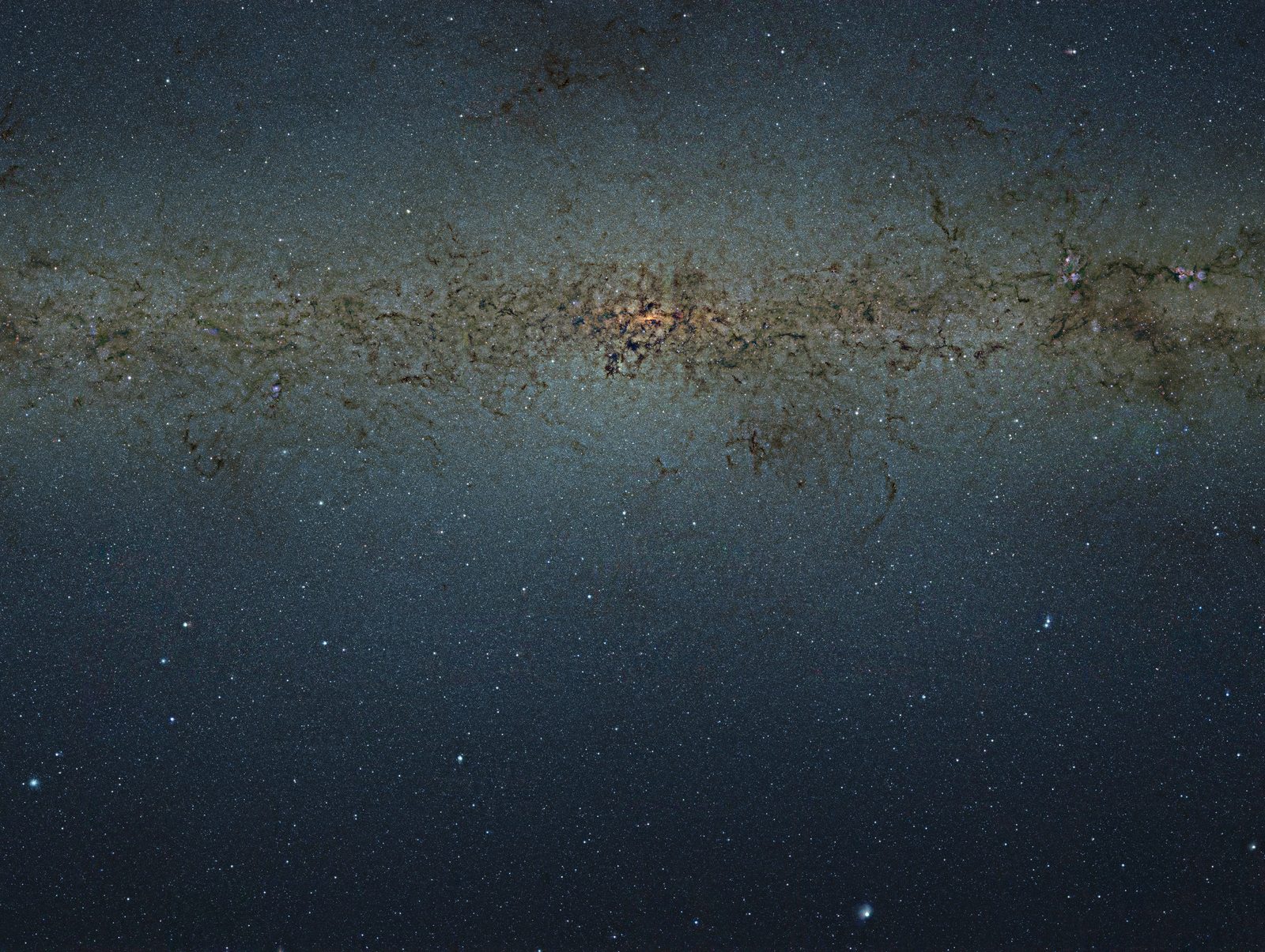 Banda luminosa de la Vía Láctea vista de canto, con el bulbo central anaranjado y vetas oscuras de polvo cruzándola sobre un fondo azulado sembrado de estrellas.