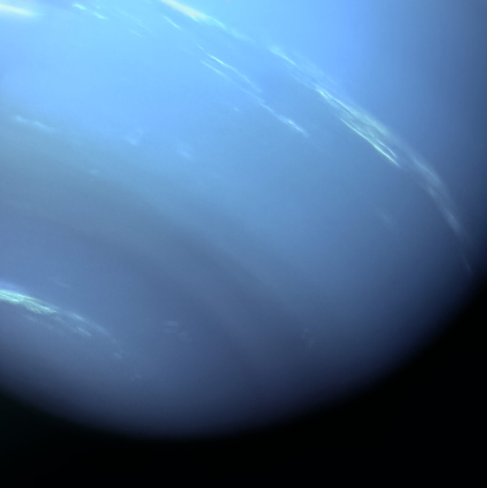 El limbo sur de Neptuno en primer plano, de un azul intenso que se apaga hacia la sombra del borde, con estrías blancas de nube alargadas cruzando la parte alta.