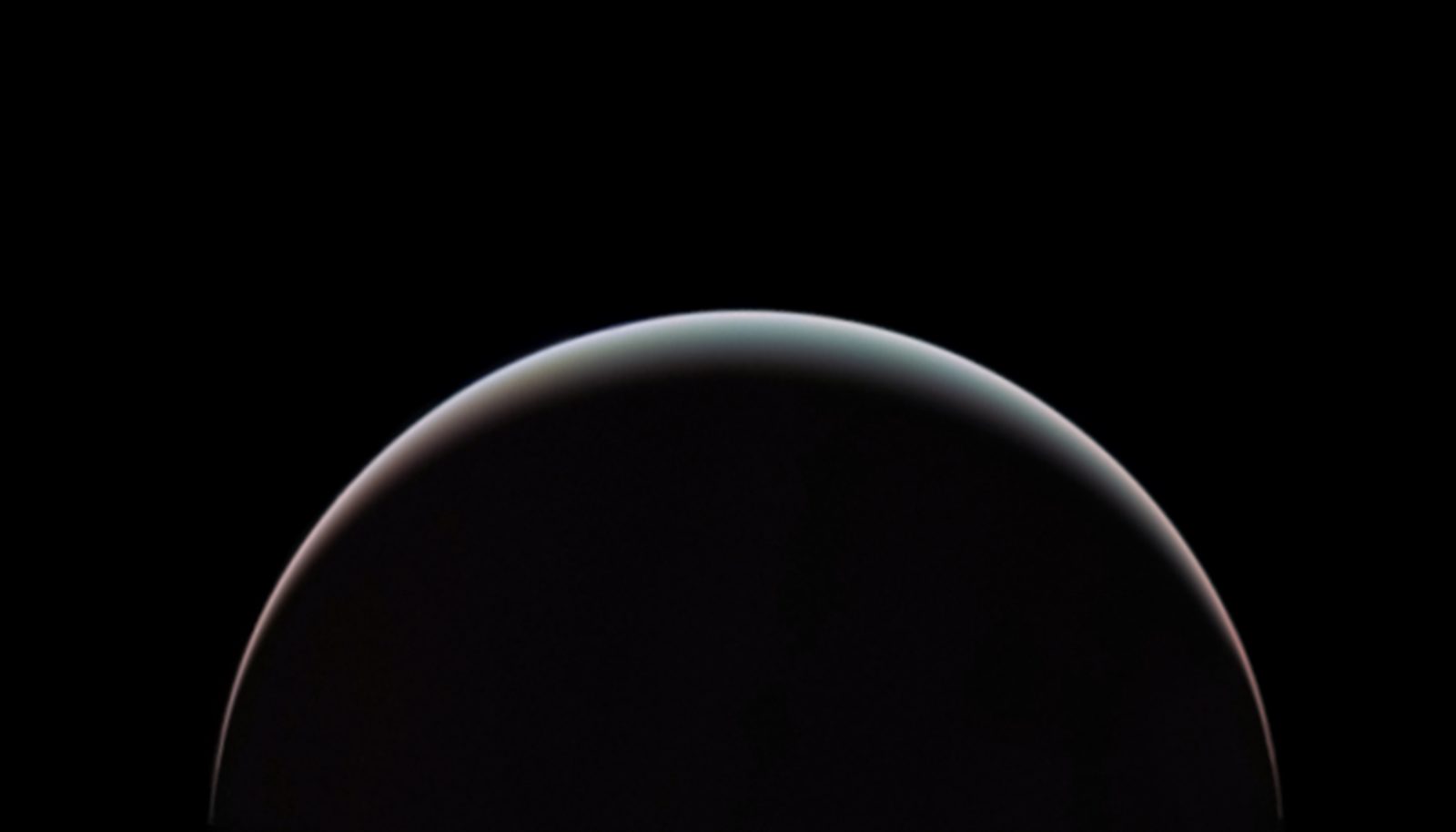 Un creciente de Urano: casi todo el planeta en sombra, sobre fondo negro, y solo un filo iluminado en el borde superior, de un azul verdoso que vira a rosado en los extremos.