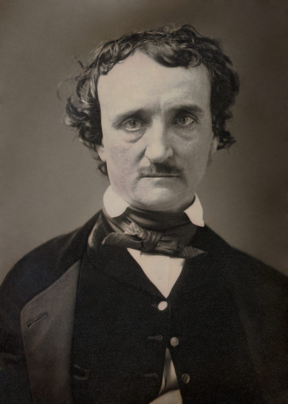 Retrato frontal en blanco y negro de un hombre de bigote, con el pelo oscuro y revuelto, sobre un fondo gris.