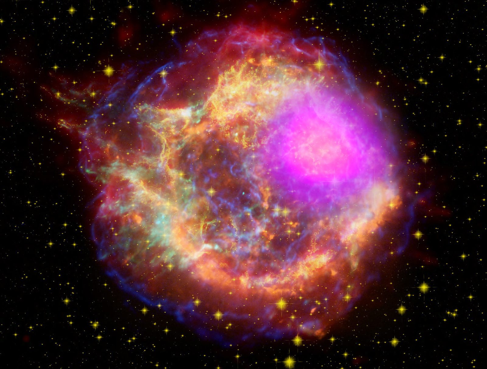 La cáscara desgarrada de una estrella reventada, con filamentos en magenta, azul, amarillo y rojo sobre fondo negro.