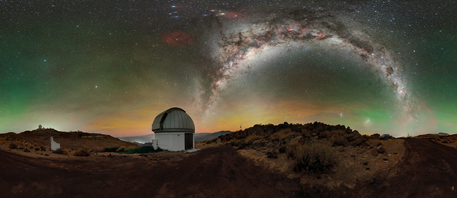 La Vía Láctea se alza desde el horizonte sobre las cúpulas de un observatorio, con el cielo teñido de verde y de rojo.