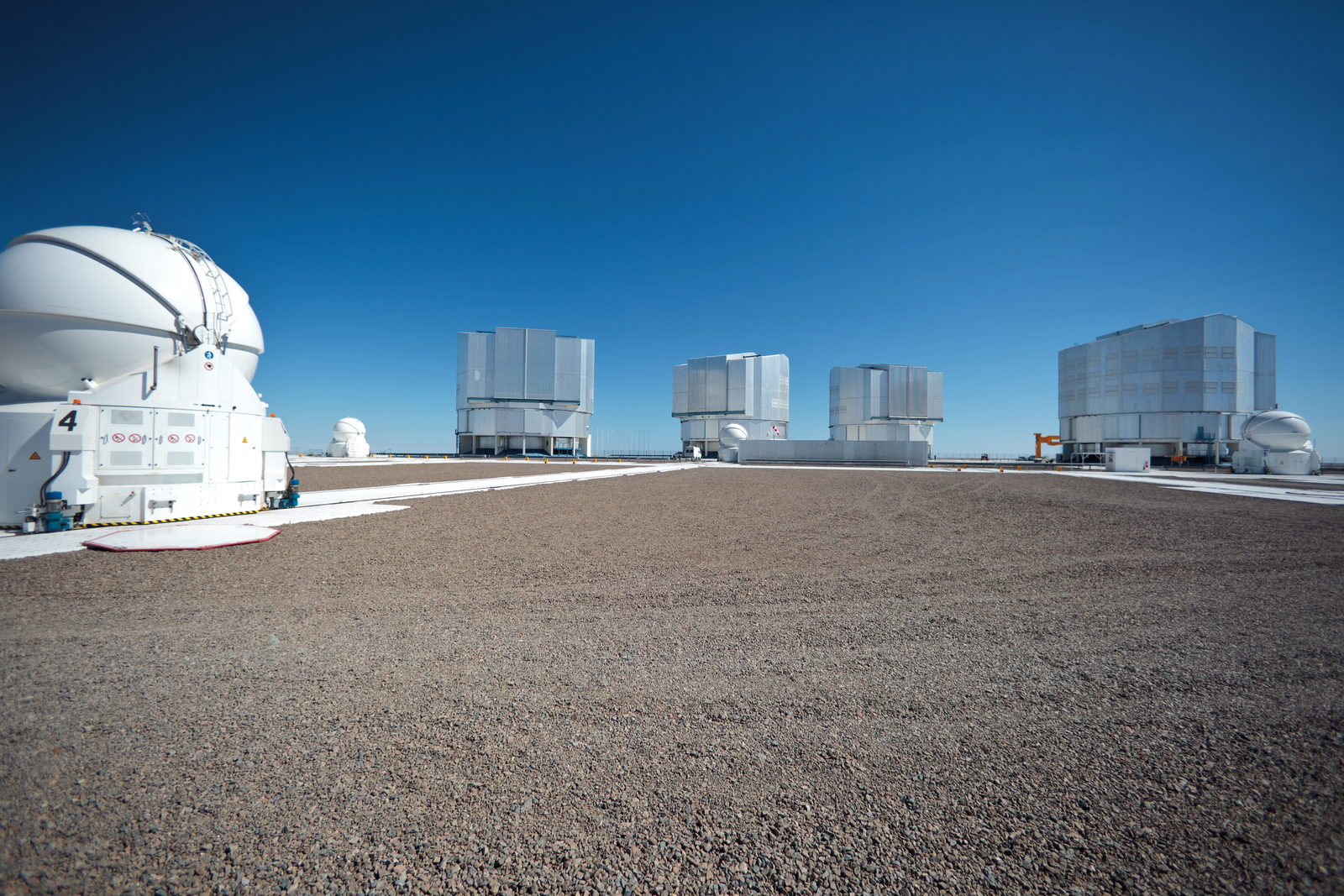 Cuatro edificios cilíndricos de telescopio sobre una montaña pelada, bajo un cielo despejado.