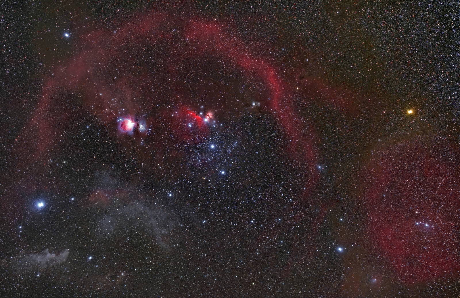 La constelación de Orión en campo ancho: el cinturón de tres estrellas en el centro, Betelgeuse anaranjada a un lado, Rigel azulada al otro, y un arco de gas rojo rodeándolo todo.